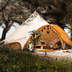 a tent is set up in the middle of some trees and bushes, with an outside seating area