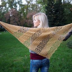 a woman is standing in the grass with a knitted shawl