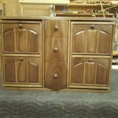 a large wooden cabinet sitting on top of a floor next to a pile of wood