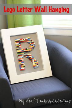 a lego letter wall hanging in a white frame on a blue chair next to a window