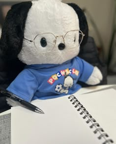 a stuffed animal with glasses and a t - shirt sitting next to a notepad