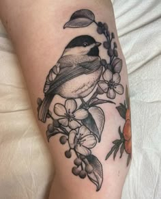 a bird sitting on top of a branch with leaves and flowers around its neck tattoo