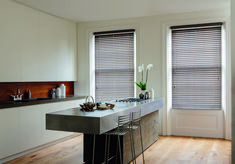 a kitchen with white walls and wooden flooring next to two windows covered in blinds