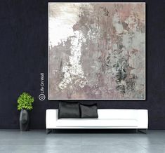 an abstract painting hangs on the wall next to a white couch and potted plant