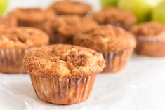 several muffins sitting on top of white paper next to green apples