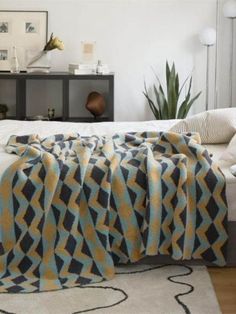 a bed with a blanket on top of it next to a potted plant in the corner