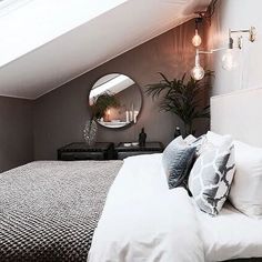 a bed sitting under a window next to a mirror and dresser in a room with white walls