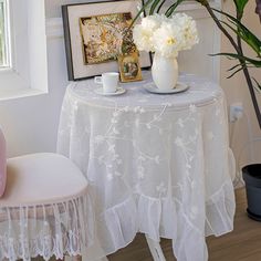 a white table topped with a vase filled with flowers next to a chair and window