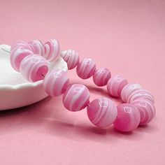 a pink and white bead necklace next to a bowl on a pink surface with a spoon