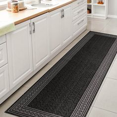 a black rug in a kitchen next to a sink and counter top with white cabinets