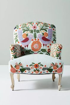 an upholstered chair with birds and flowers on the back, sitting against a white wall