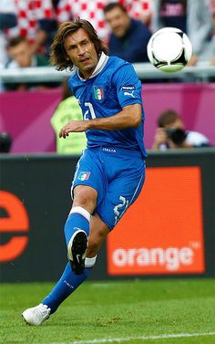 a man kicking a soccer ball on top of a field with people in the background