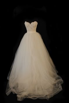 a white wedding dress on display in front of a black background