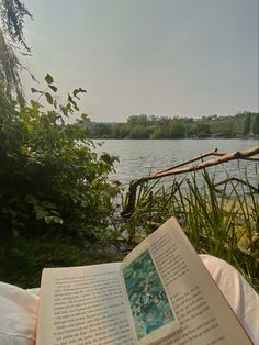 an open book sitting on top of a bed next to a lake