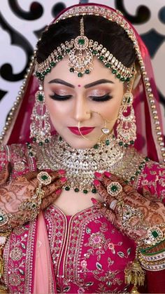 a woman in a pink bridal outfit with jewelry on her head and hands behind her neck