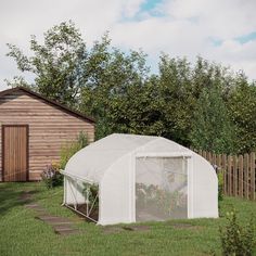 a small white tent in the grass next to a wooden fence and shed with flowers growing inside