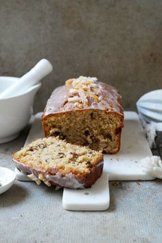 a loaf of banana bread sitting on top of a cutting board next to a bowl