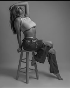 a woman sitting on top of a wooden stool wearing high waisted jeans and a white crop top