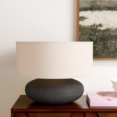 a table lamp sitting on top of a wooden dresser next to a painting and vase