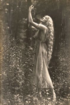 an old photo of a woman with long hair holding a bird in her hand while standing in the woods