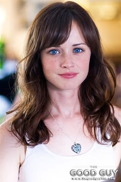 a beautiful young woman wearing a white tank top and blue eyes posing for the camera