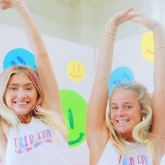 two women in white shirts standing next to each other with their hands up and smiling