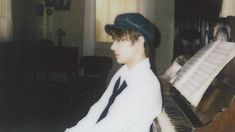 a young man sitting at a piano wearing a hat