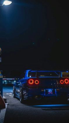 a blue car parked on the side of a road at night with its lights on