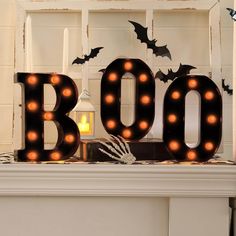 a lighted boo sign sitting on top of a mantle next to a candle and some bats