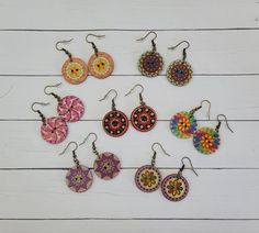 six pairs of earrings are shown on a white wooden surface, each with different designs and colors