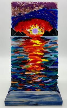 Presenting a Handmade Glass Fused Sunset - a 12x6 masterpiece in impressionist style, capturing the brilliance of a sunset reflecting on the ocean.  Enjoy breathtaking hues of a radiant sunset as depicted in this unique glass fusion artwork. The brilliant colors, meticulously fused together, capture the essence of the impressionist style, creating a harmonious blend of warm tones that dance across the glass canvas. The use of this technique lends a sense of fluidity and movement to the scene, truly bringing the sunset to life. What sets this piece apart is its ability to illuminate from behind, casting a mesmerizing glow that enhances the overall ambiance of any room. Place it near a light source, and watch as the vibrant colors come alive, creating a captivating play of light and shadow. Fused Glass Sunset, Art Sunset, On The Ocean, Glass Fusion, Fused Glass Art, Glass Art Sculpture, Glass Sculpture, Brilliant Colors, Light And Shadow