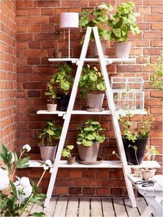 a white ladder shelf with potted plants on it in front of a brick wall