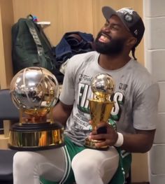 a man sitting on the floor holding two trophies