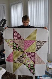 a young boy holding up a large quilt