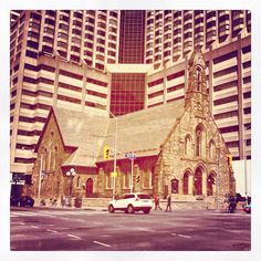 an old church sits in the middle of a city street with tall buildings behind it