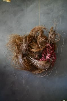 a bunch of hair hanging from a string on a gray wall next to an orange flower