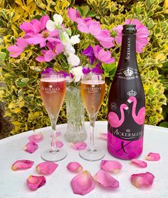 two wine glasses and a bottle sitting on a table with pink flowers in the background