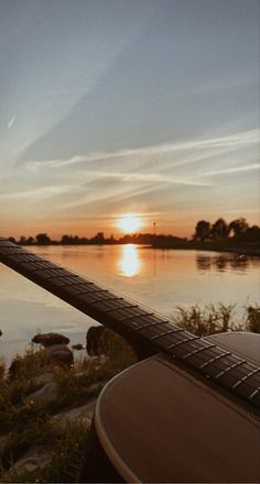 an acoustic guitar resting on the edge of a railing overlooking a body of water at sunset