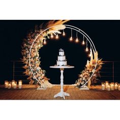 a wedding cake sits on top of a white pedestal surrounded by candles and wreaths