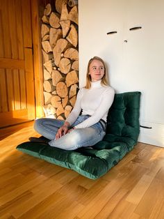 a woman sitting on top of a green chair in front of a fire place with logs behind her