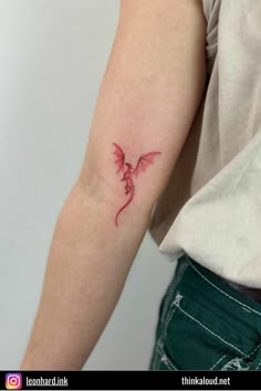 a woman's arm with a small red dragon tattoo on the left side of her arm