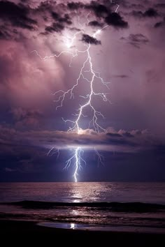 a lightning bolt is seen over the ocean on a cloudy day with dark clouds and purple hues