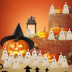 a group of white ghost candles sitting on top of a pile of hay next to pumpkins