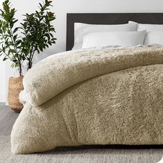 a bed with a fluffy comforter on top of it next to a potted plant