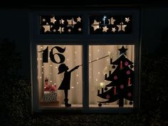 a window decorated with christmas lights and silhouettes of children in front of a tree