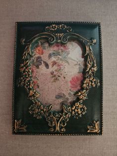 a green and gold plate with flowers on it's side, in the shape of a heart