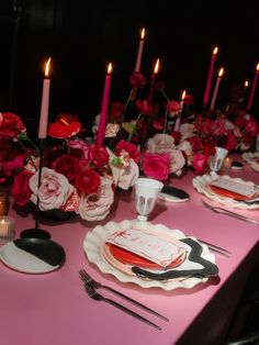 the table is set with pink and red flowers, black place settings, and candles