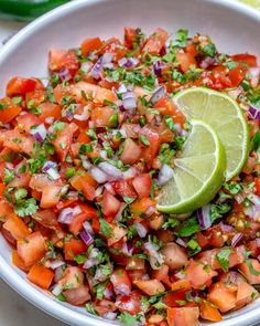 a white bowl filled with chopped up vegetables and lime wedged in the middle next to it