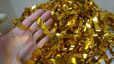 a hand is reaching up towards a pile of shiny gold foiled paper streamers