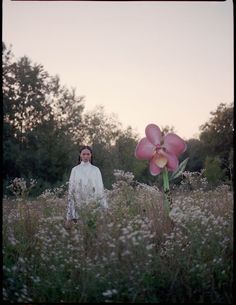 a woman standing in a field next to a large flower